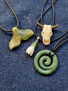A collection of hand-carved natural stone pendants including a green jade spiral, a white nephrite snowdrop, and a bull skull by Stone Flower.