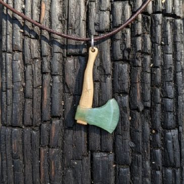 This exquisite axe pendant features a striking combination of dark nephrite and warm petrified wood. Handcrafted to highlight th…