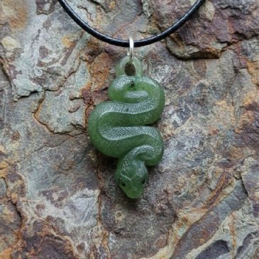 Adorn your style with this exquisite Nephrite Snake Pendant. Expertly carved from deep green jade, it features striking red garn…