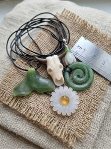 A collection of hand-carved natural stone pendants including a green jade spiral, a white nephrite snowdrop, and a bull skull by Stone Flower.