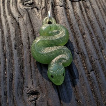 This exquisite Nephrite Snake Pendant features deep green stone expertly carved into a fluid silhouette. Piercing red garnet eye…