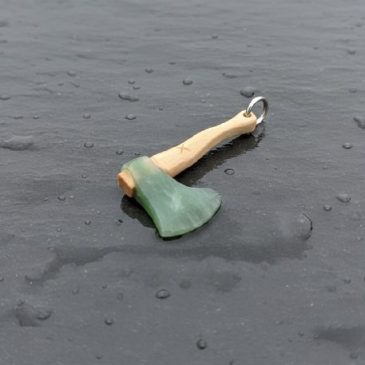 This handcrafted axe pendant features a striking contrast between deep green nephrite and the earthy tones of petrified wood. A …